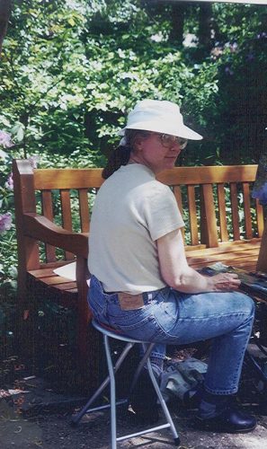 Me wearing a white sun hat, and blue jeans (my typical gear) sitting in waterlilies painting in this lush garden.
