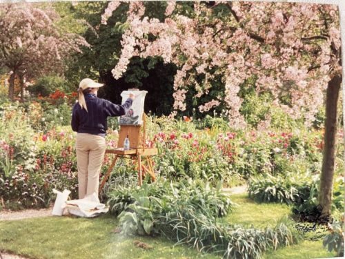 Me standing in a Monet's garden painting one of the many paintings I did there, surrounded by a lush garden in the spring while the cherry blossom pink flowers surround me with  their spring show.