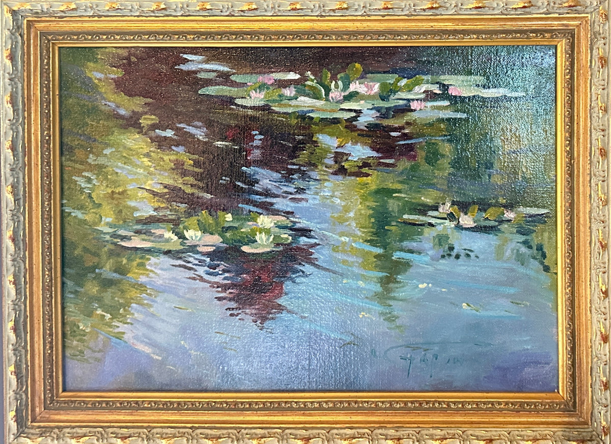 A framed impressionist oil painting , Monet's Waterlilies 1, depicting water lilies in Monet's Garden , housed in ornate French gold frame. The painting features blue water, green and yellow reflections, and pink and white lily pads, with a signature in the lower right corner.